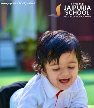 Smiling toddler in a white shirt playing outdoors, with the Jaipuri School logo and website in the top right corner.